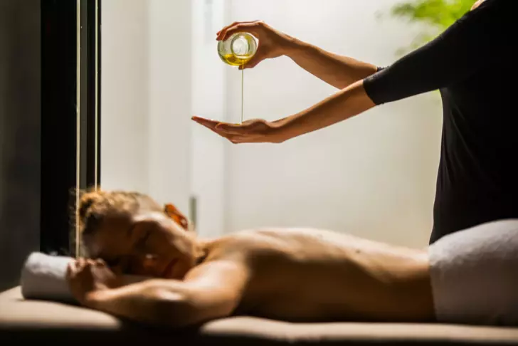 A woman pouring oil into another person's hand indoors.