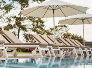 Sun loungers and parasols by the pool, framed by lush greenery and a bright sky.