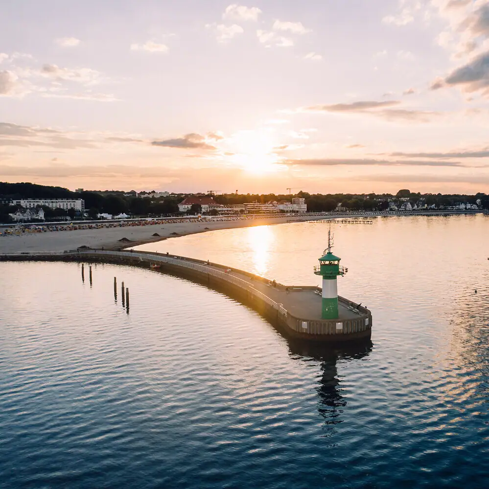 A pier with a lighthouse extending over a calm body of water under a partly cloudy sky.