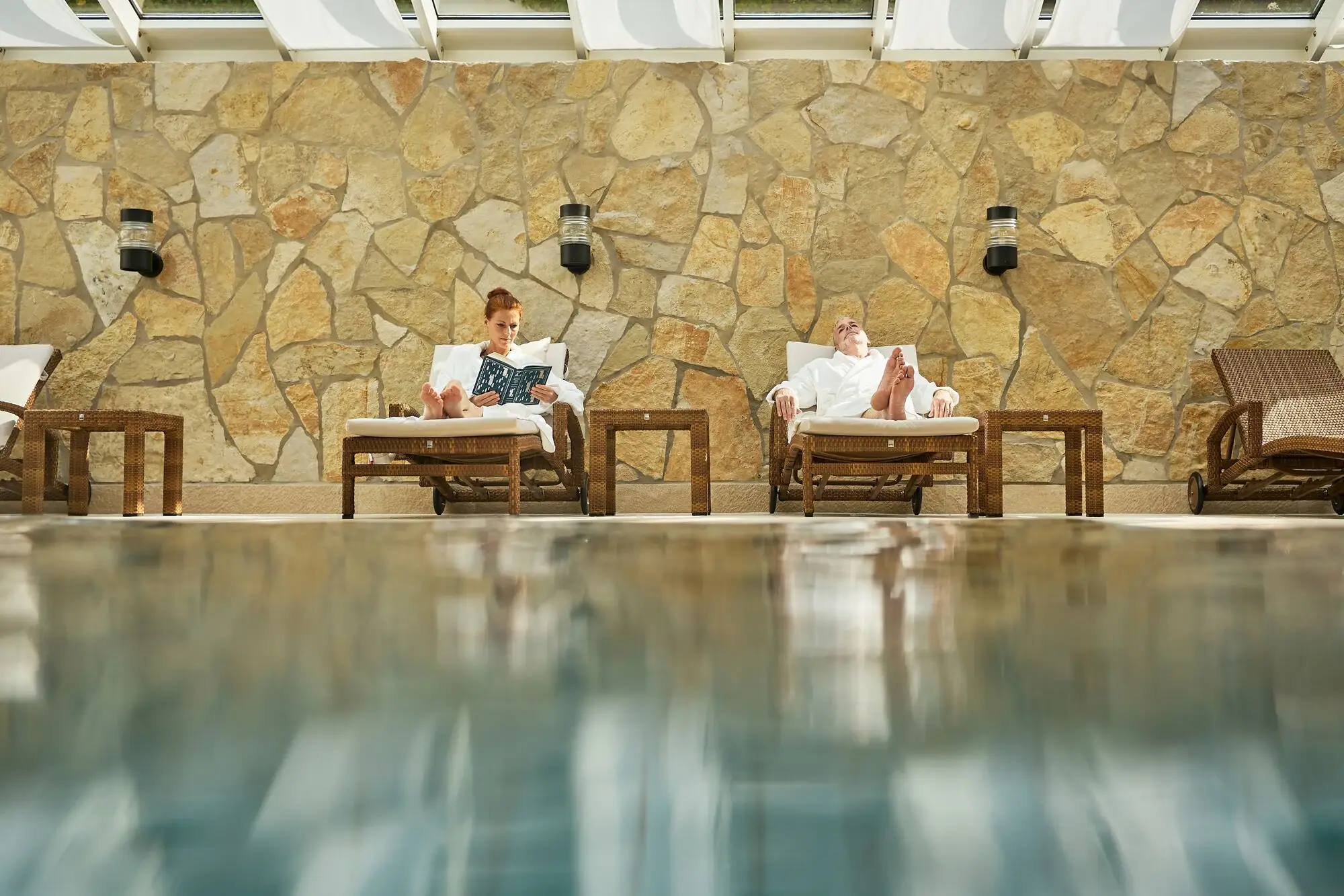 A man and woman sitting in chairs by a pool.