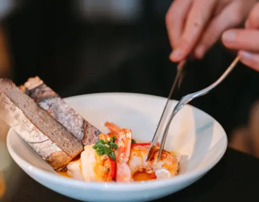 A person holds a pair of tongs over a bowl of food.