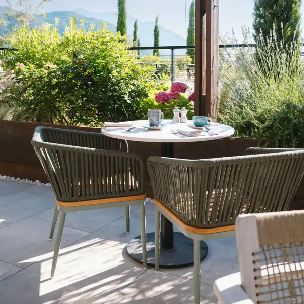 A breakfast table in the morning sun with pink flowers on it and a view of the green landscape