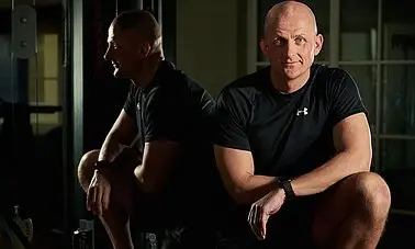 a man in black workout clothes sits leaning on his knee in front of a mirror. 