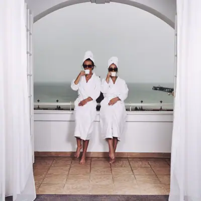 Two women wearing white robes and towels sitting on a window sill.