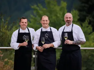 Group of men in black aprons holding wine glasses.