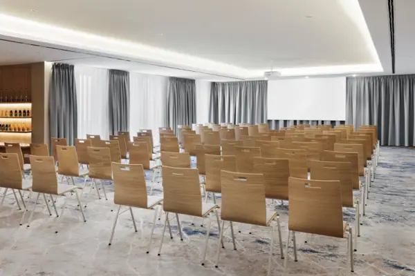 Conference Room 1 at the A-ROSA Tegernsee, with rows of chairs, a projector and a screen.