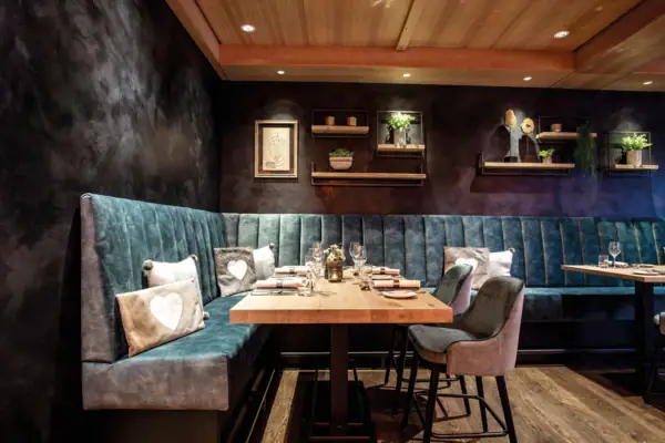 Ein Tisch mit Stühlen und einer gepolsterten Sitzbank, darauf Teller und Gläser, in einem stilvoll eingerichteten Raum.