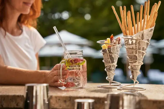 Woman holding a glass of water with fruit at an outdoor bar counter.