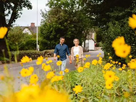 A couple is walking through the streets of a small town and are slightly covered by yellow flowers. 