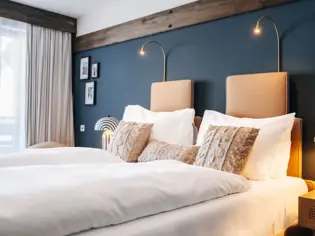 Cozy hotel room featuring a neatly made bed with plush pillows and a stylish wall-mounted lamp.