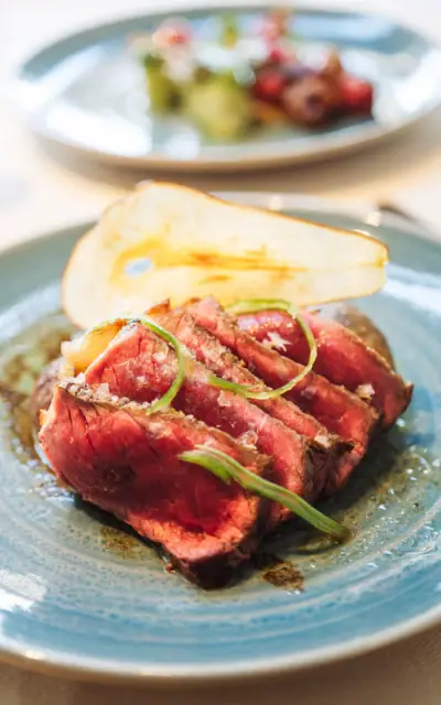 A gourmet dish featuring a beautifully presented piece of red meat with garnishes on a white plate.
