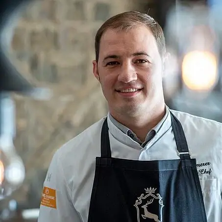 A man in a black apron smiling indoors.