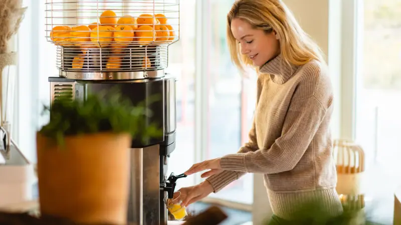 Breakfast at A--ROSA Sylt A woman is pouring orange juice from a juice dispenser.