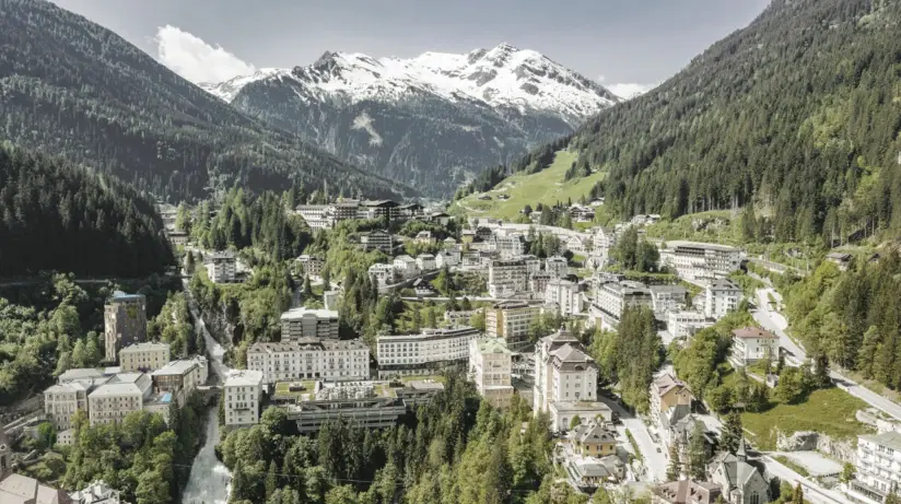 Town in the mountains with surrounding wooded slopes and snow-capped peaks.