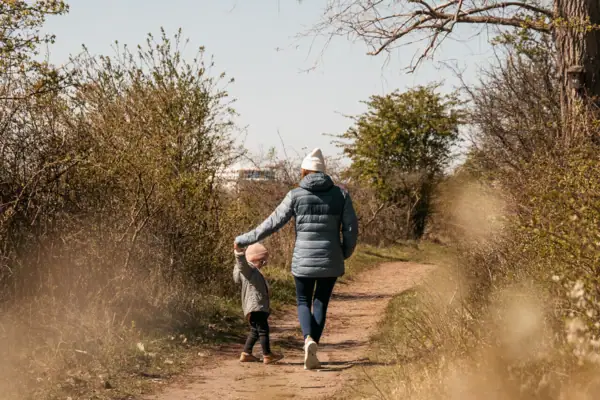 Eine Frau und ein Kind gehen auf einem Erdweg spazieren.