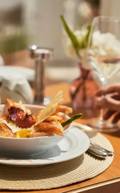 A bowl of shrimp served on a plate, accompanied by a wine glass on a table.