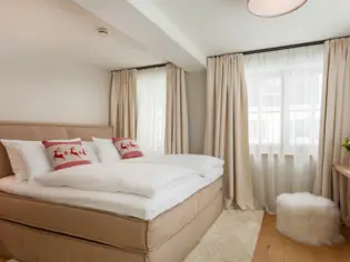 A beige upholstered bed stands against a white wall with white bed linen and two Christmas decorative cushions with reindeer on them.