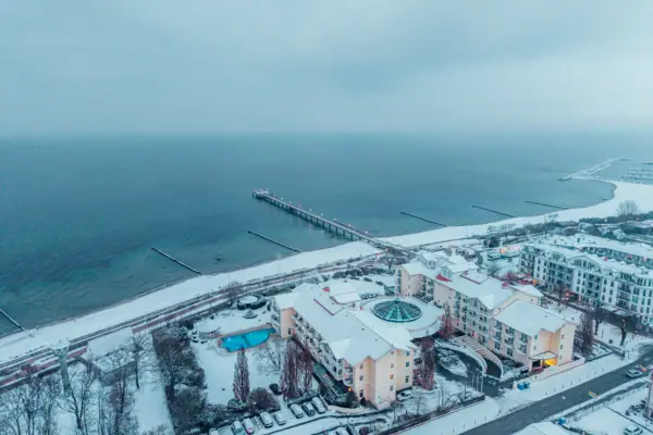 Snow-covered beach with buildings and a pier in winter.