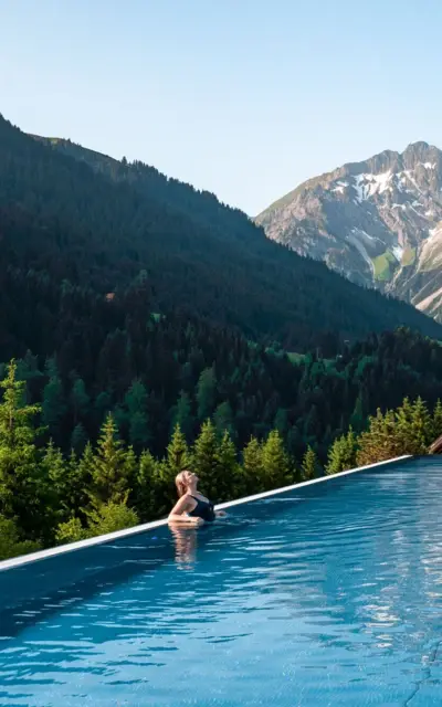 Woman leaning on the edge of an infinity pool with a mountain backdrop.