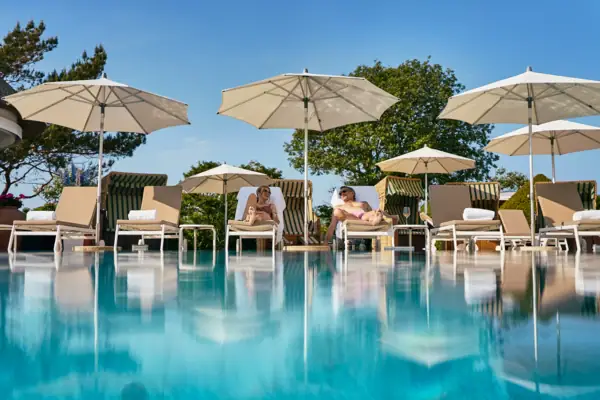 A group of people sitting in chairs by a swimming pool under umbrellas.