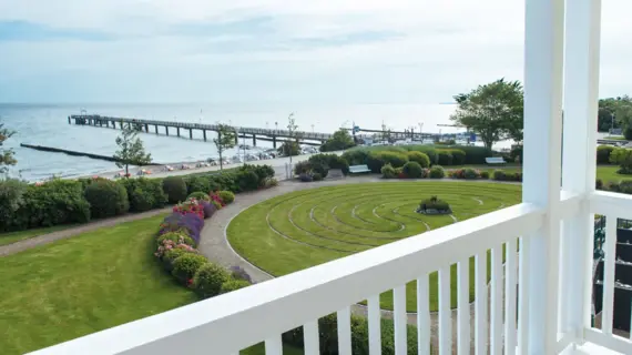 View from a balcony of a garden and a pier jutting out into the Baltic Sea.