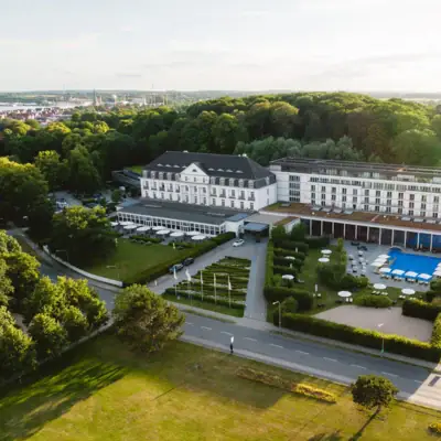 Großes weißes Gebäude mit Pool und Bäumen im Vordergrund.
