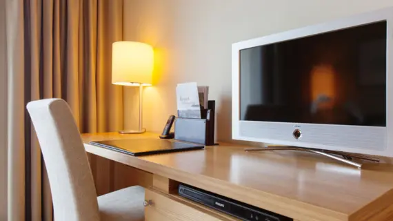 A light-colored chair stands in front of a desk with a small television, a telephone and some flyers.