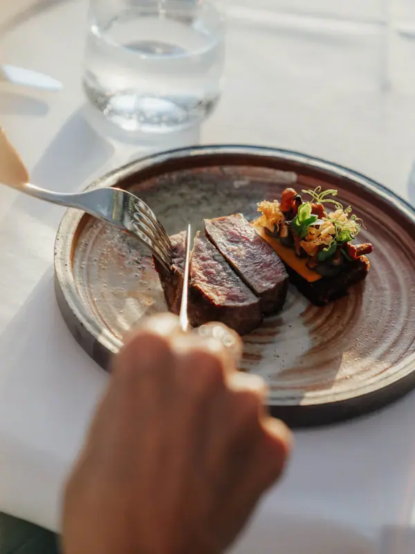 One person cuts meat on a plate.