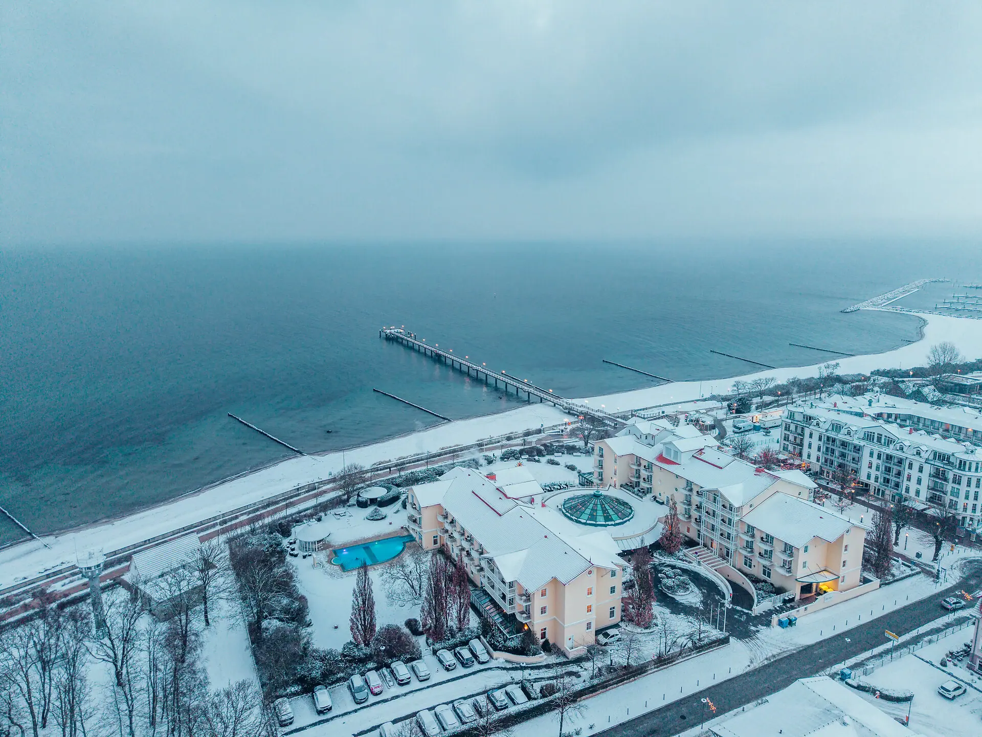 A snow-covered beach with buildings and a pier in winter.