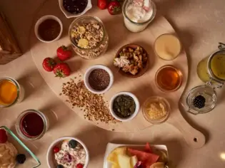 Table with various breakfast components for a muesli, in small bowls on a wooden board.