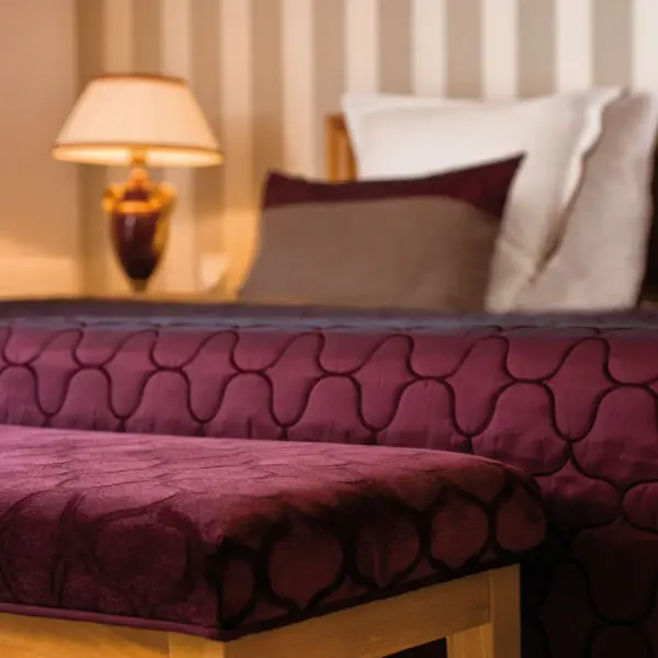 Close-up of a bed with a burgundy ceiling and a lamp in a hotel room.