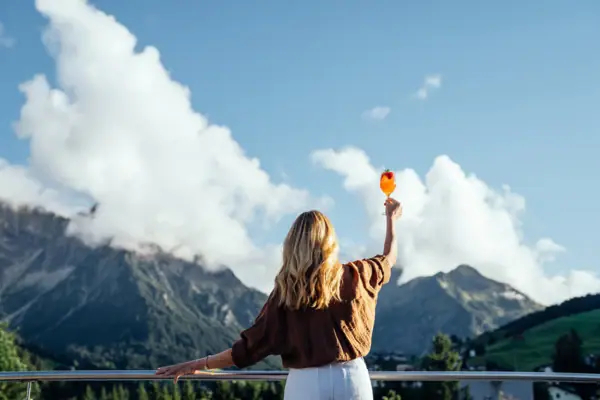 A woman is holding a drink aloft and looking at the mountains.