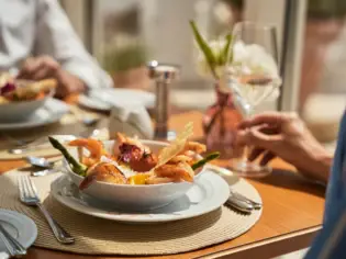 A bowl of prawns on a plate, surrounded by crockery and a wine glass.