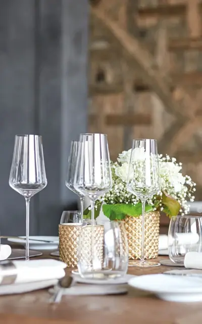 Elegantly laid table with wine glasses and flower vase as centerpiece.