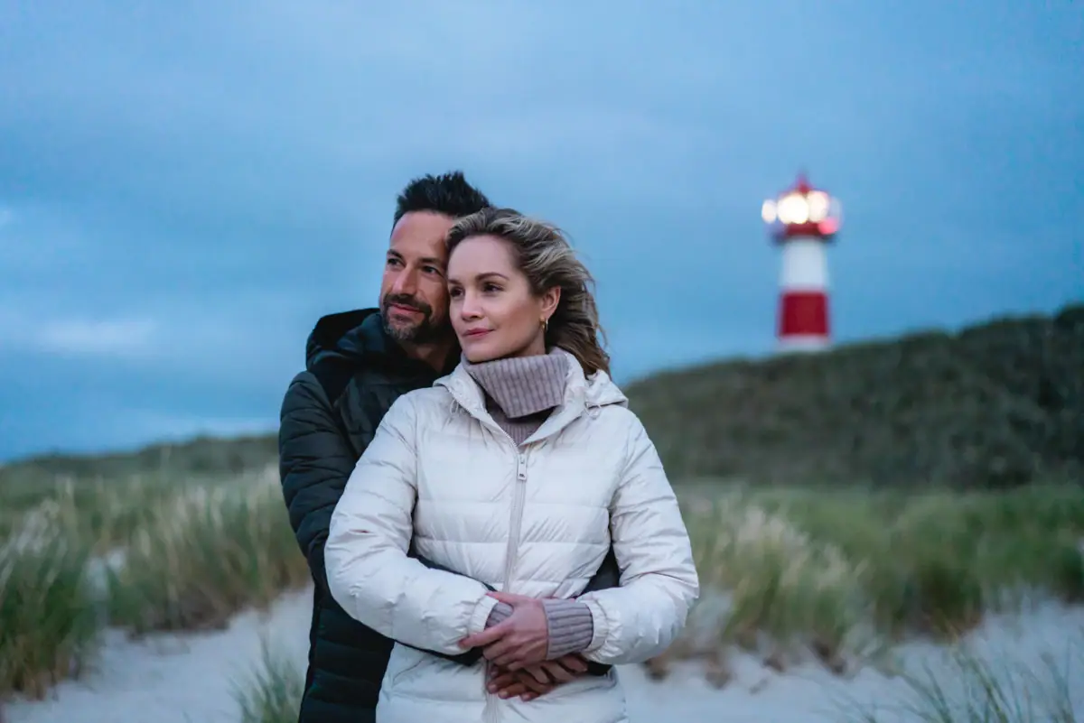 A man and woman standing on a beach with a lighthouse in the background.