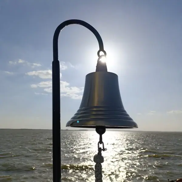 Eine Glocke an einem Pfosten mit Sonnenschein am Himmel.