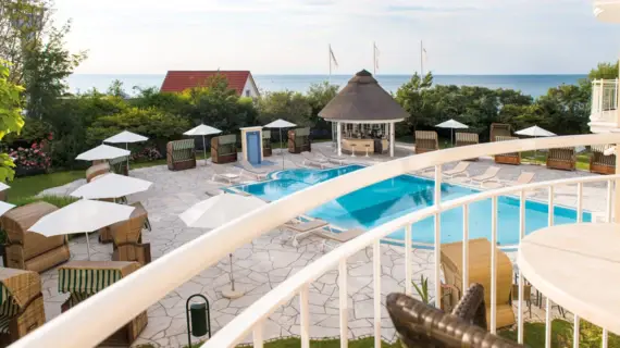 View from a balcony of a pool with sun loungers and parasols on the beach.