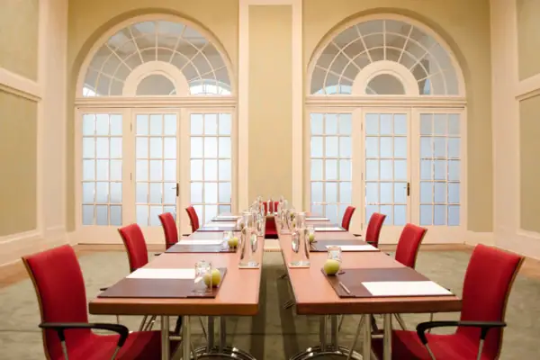 Grüner Saal Ein langer Tisch mit roten Stühlen in einem Tagungsraum.