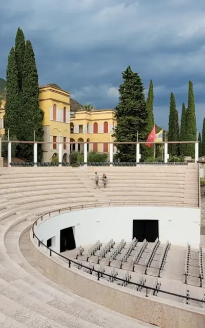 A large outdoor theater with stairs and people in front of it under a clear sky.