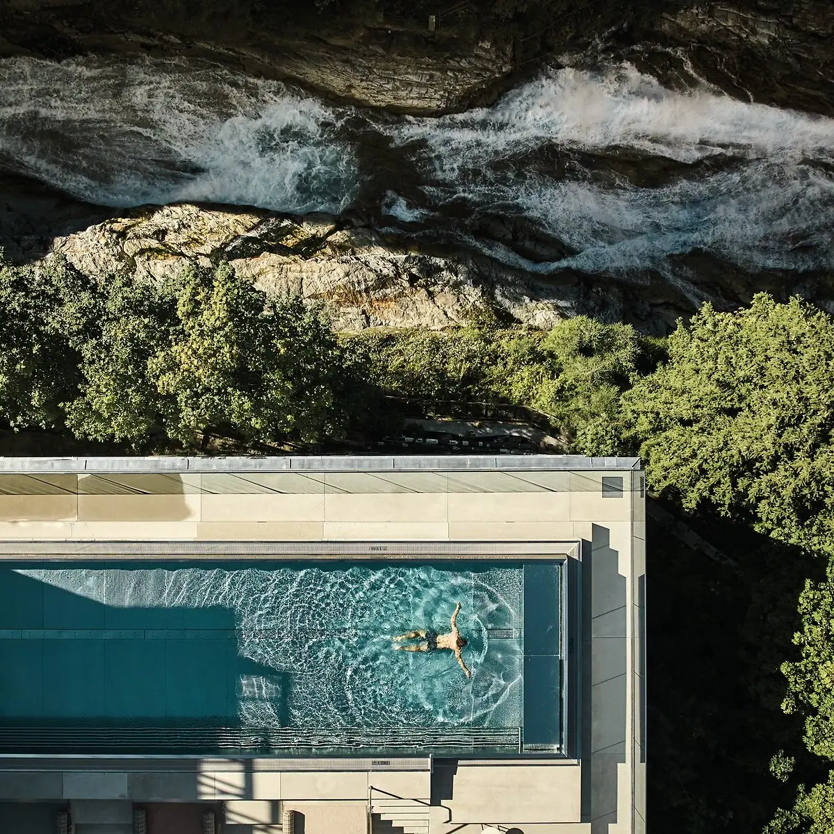 A person is swimming in the pool at the A-ROSA Straubinger Grand Hotel Bad Gastein, next to the Gastein Waterfall.