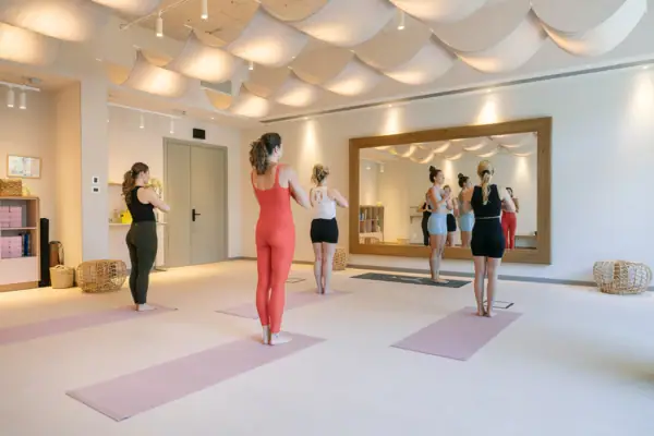 Mehrere Gäste beim Yoga im lichtdurchfluteten Studio des A-ROSA Gardasee mit großen Spiegeln und warmem Ambiente.