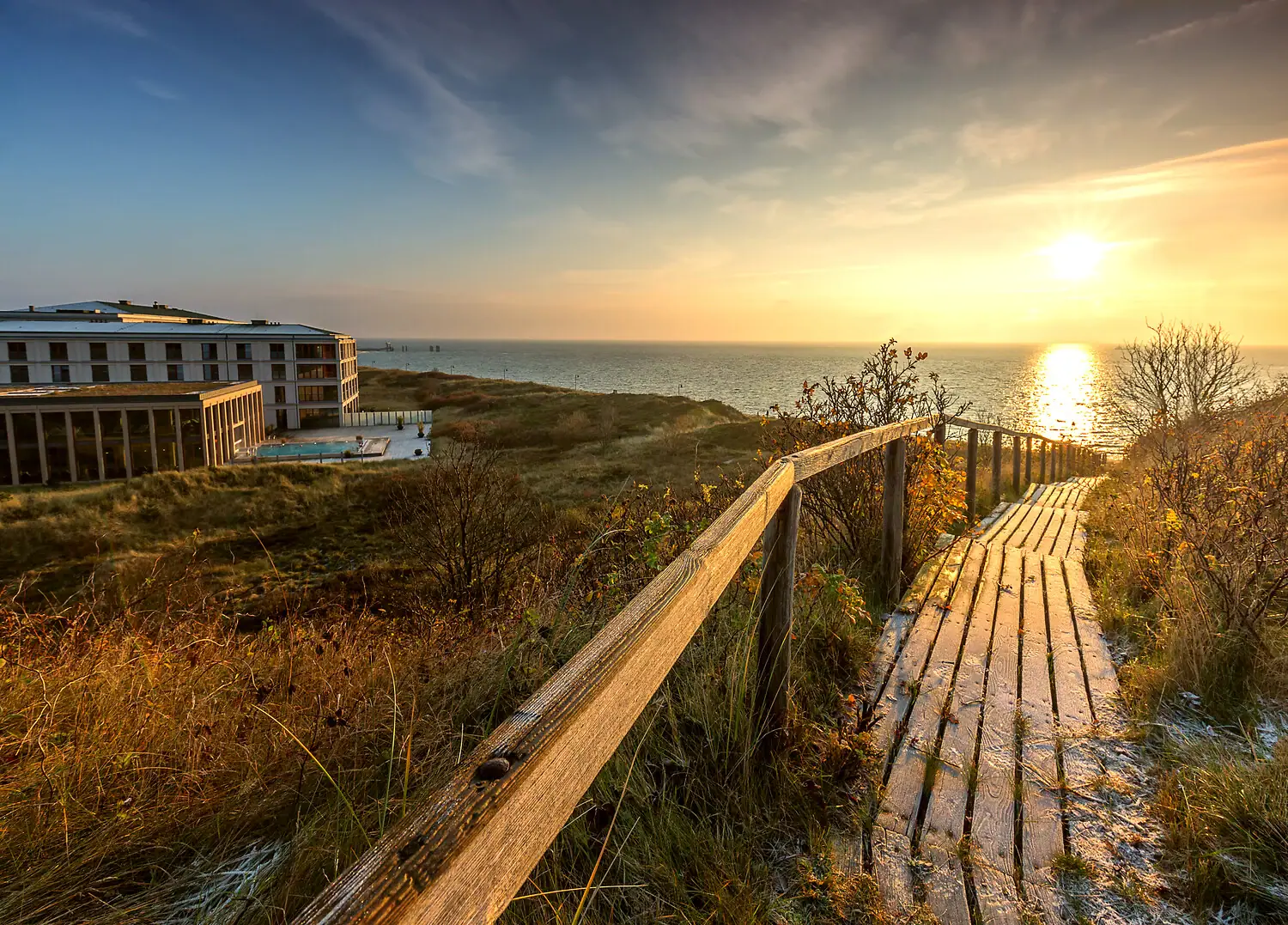 Wooden walkway leads to the beach with buildings and water in the background.