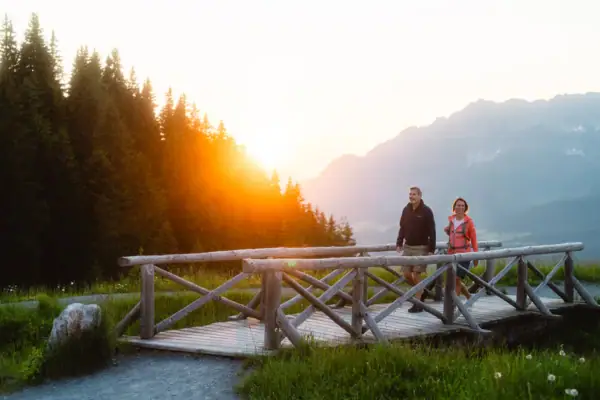 Ein Mann und eine Frau gehen auf einer Holzbrücke über einen See.