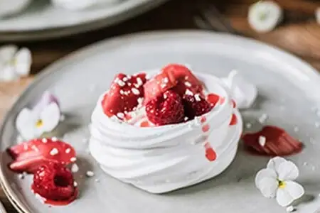 Ein Teller mit Dessert, verziert mit Beeren und Sahne, auf einem Tisch.