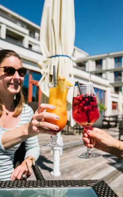 Two women sitting outside, holding up their orange and red cocktails for a toast. 