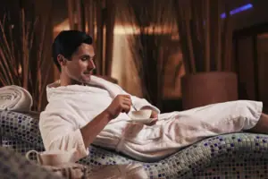 A man in a bathrobe holds a bowl of tea.