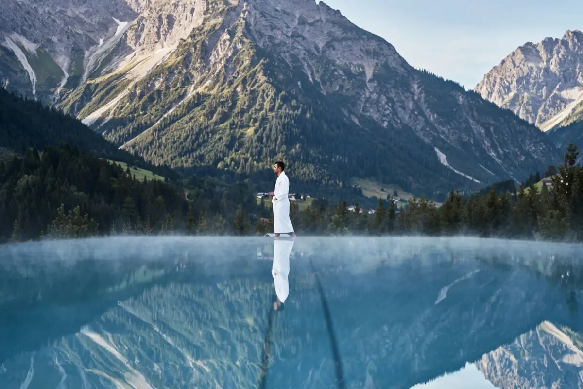 Ein Mann steht in einem Wasserbecken mit Bergen im Hintergrund.