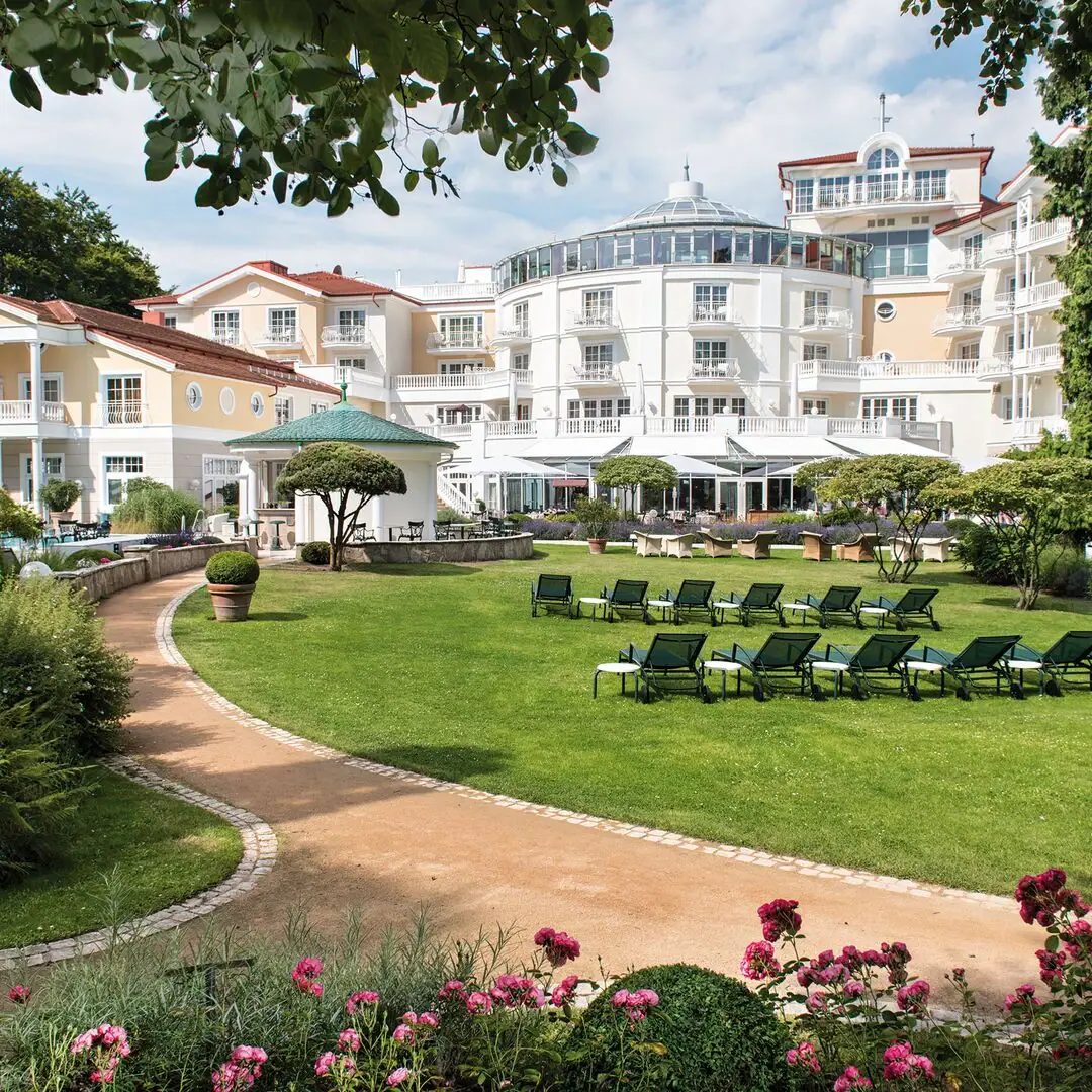 Liegestuhl im Garten mit Bäumen und klarem Himmel im Hintergrund.