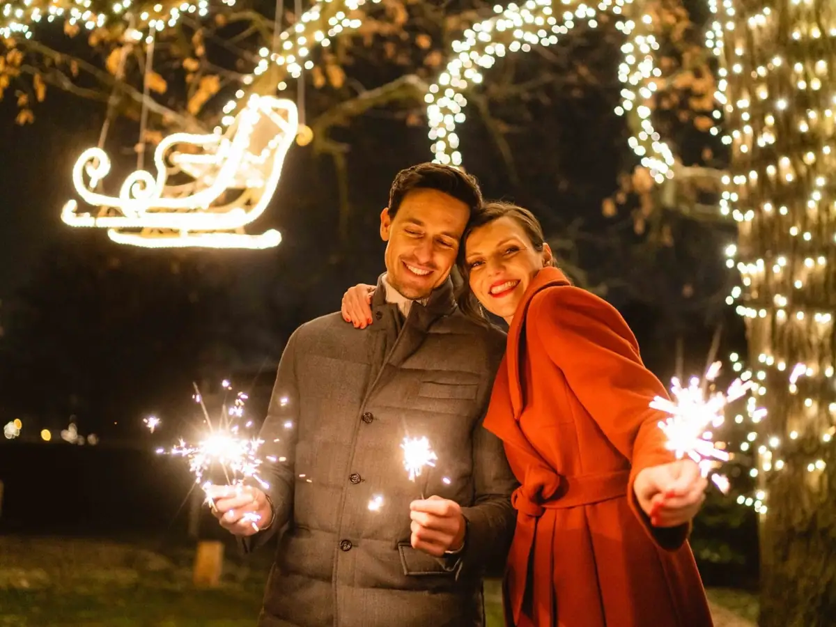 NYE A man and woman holding sparklers with smiles in front of trees.