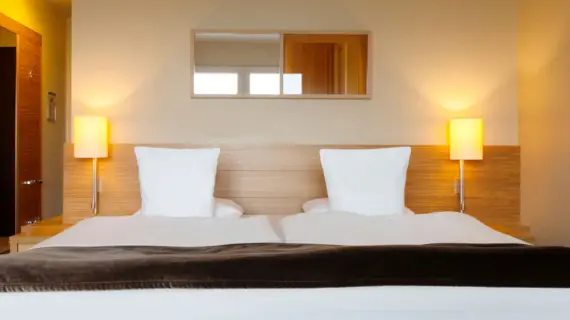 A hotel bed photographed from the front with two lights on the left and right above the bedside tables.